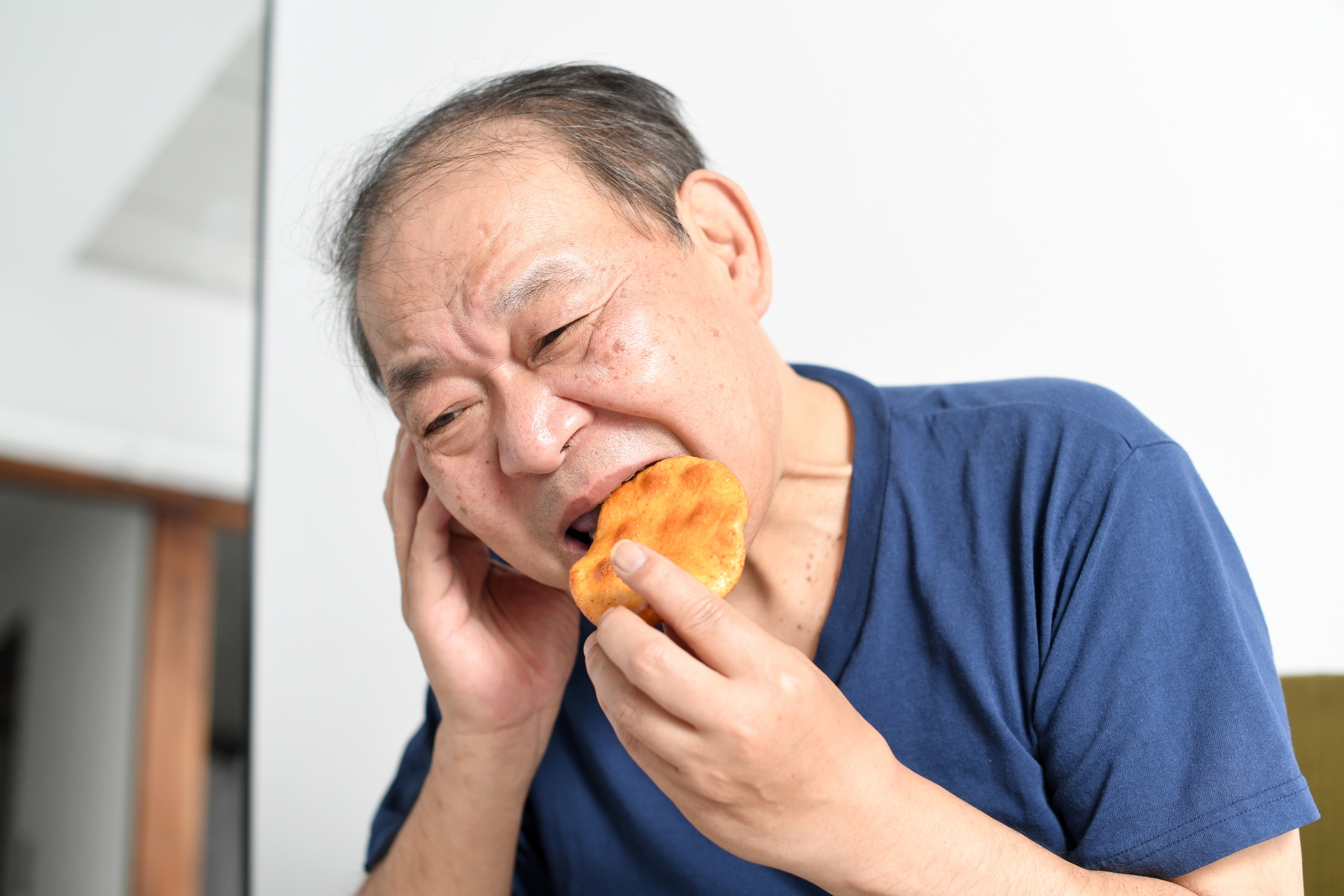 辛い顔で煎餅を食べる高齢者男性